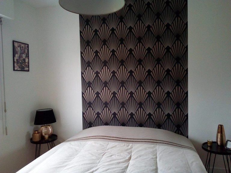 Panneau Art déco noir et cuivre encadrant le lit, lampe et chevet noirs