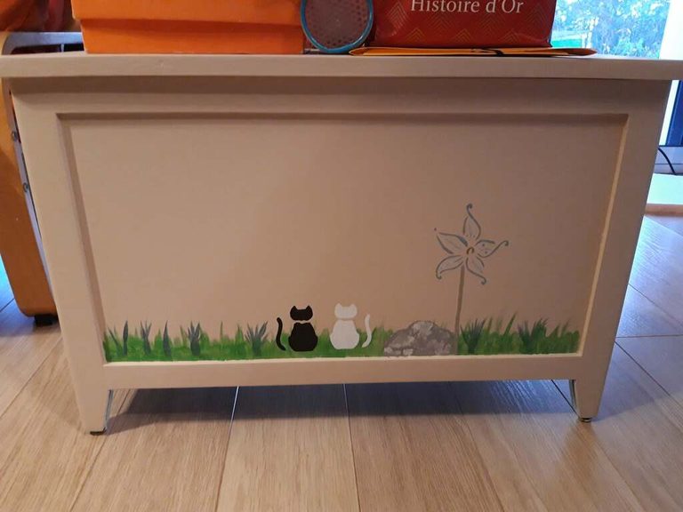 Coffre à jouets repeint en crème, façade décorée au pochoir d'herbe et de deux chats